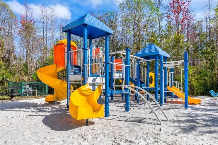 Blue and Yellow Playground on Sand with Building Exterior and Trees in the Background